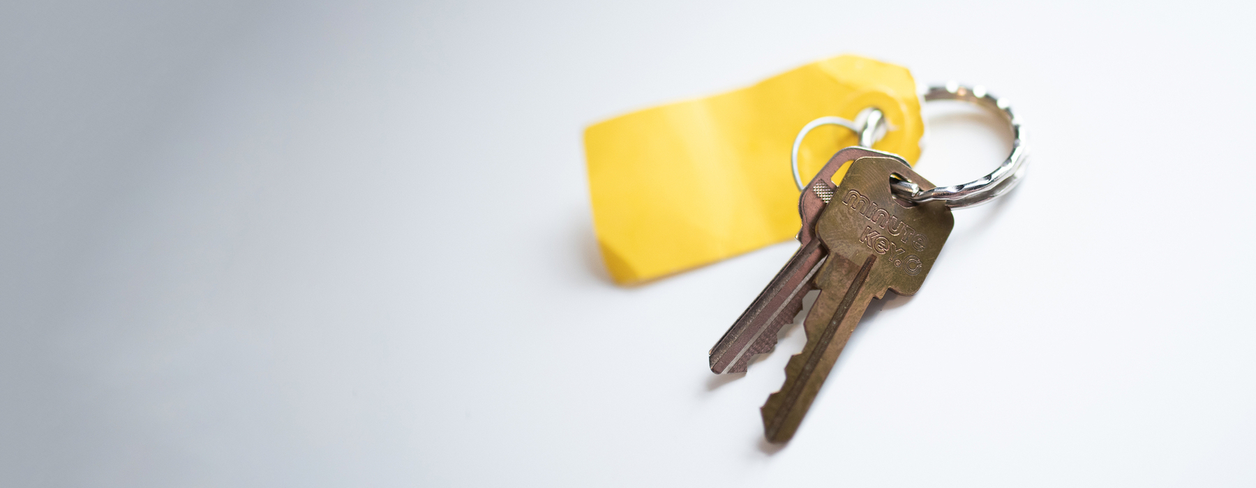 A keychain with two keys and one yellow tag sitting on a white background